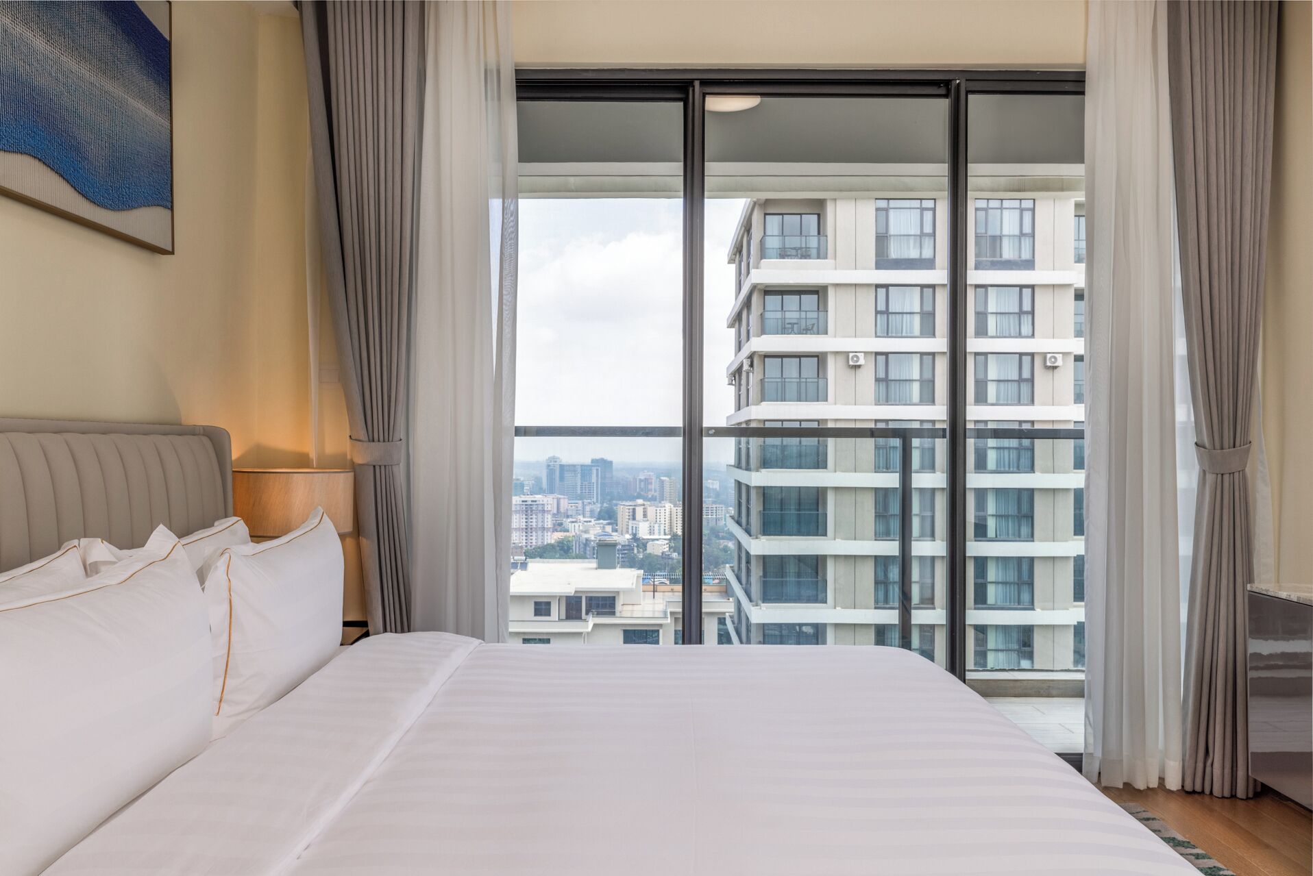A hotel room with a large bed, a view of a cityscape through floor-to-ceiling windows, and a modern design.