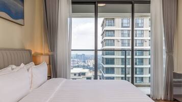 A hotel room with a large bed, a view of a cityscape through floor-to-ceiling windows, and a modern design.