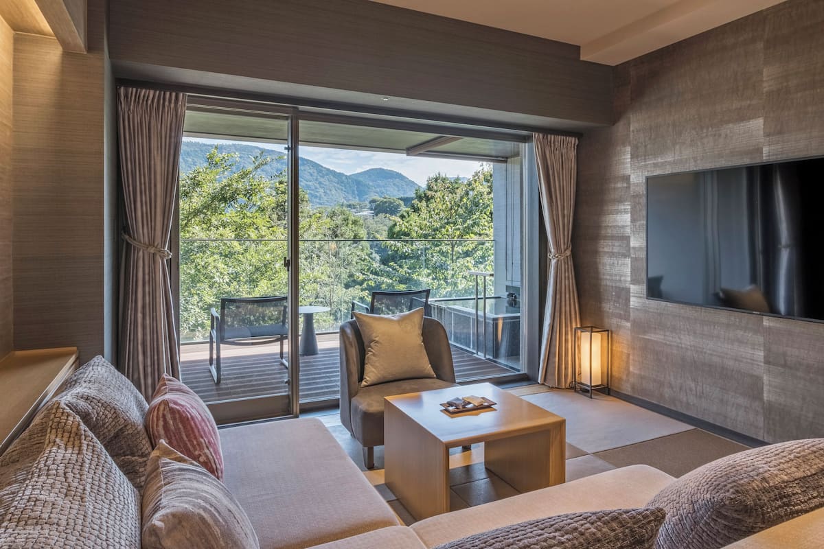 Ett modernt hotellrum med en soffa, ett litet bord, en TV och en balkong med utsikt över bergen.