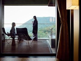 Un balcón con vistas a un paisaje montañoso, una mesa con sillas y una persona de pie.