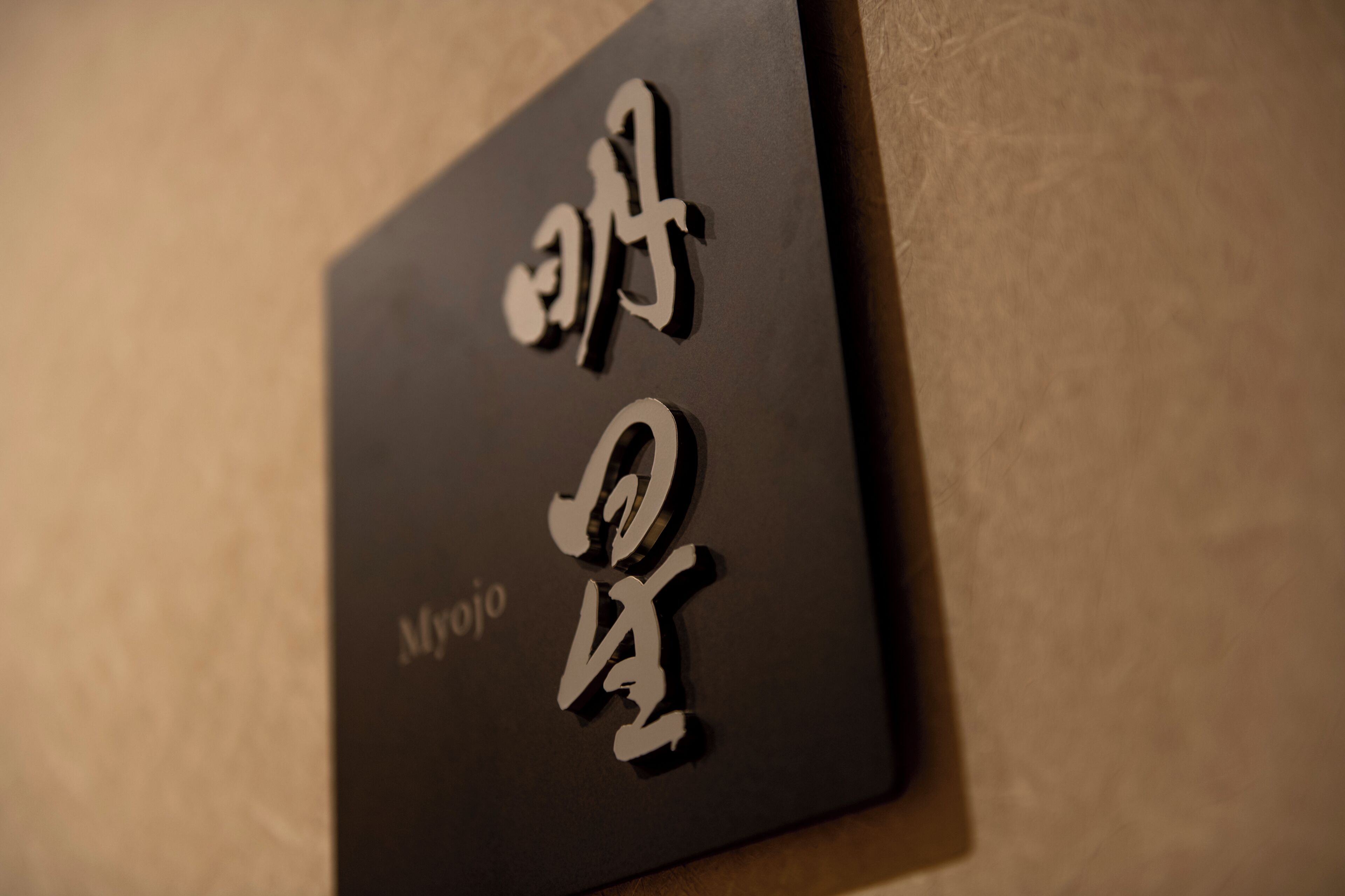 A black sign with white Japanese characters and the word "Myojo" on it.