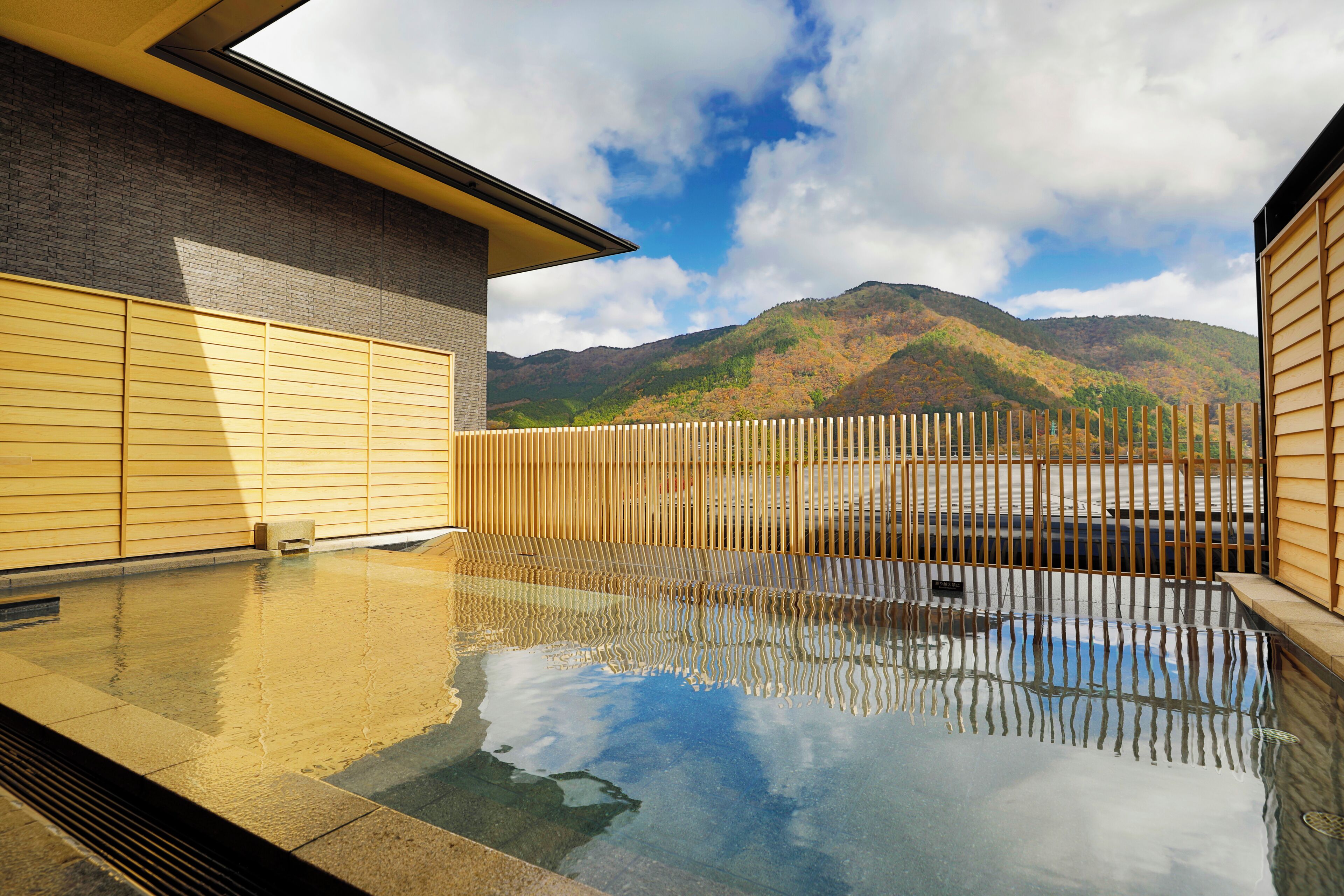 A modern building with a pool reflecting the sky and mountains.