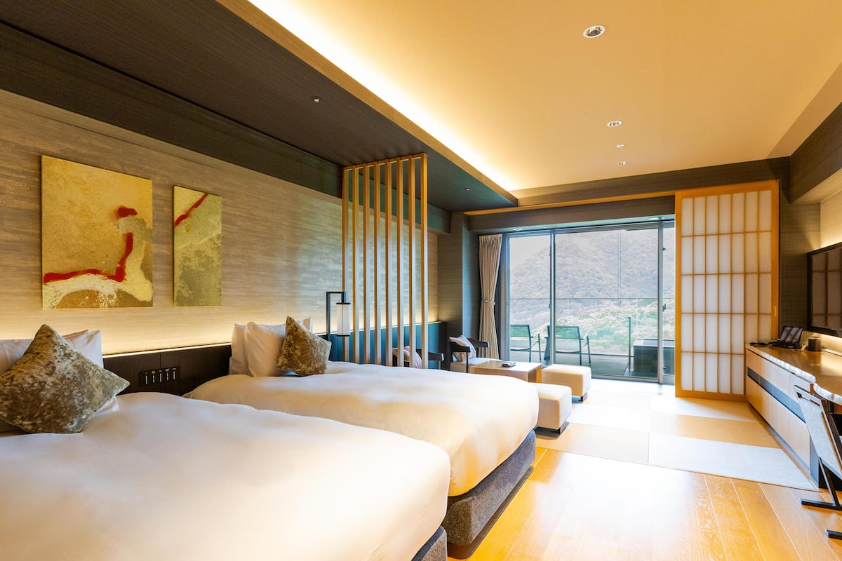 Ett modernt hotellrum med två sängar, ett skrivbord och ett stort fönster med utsikt över omgivningarna.