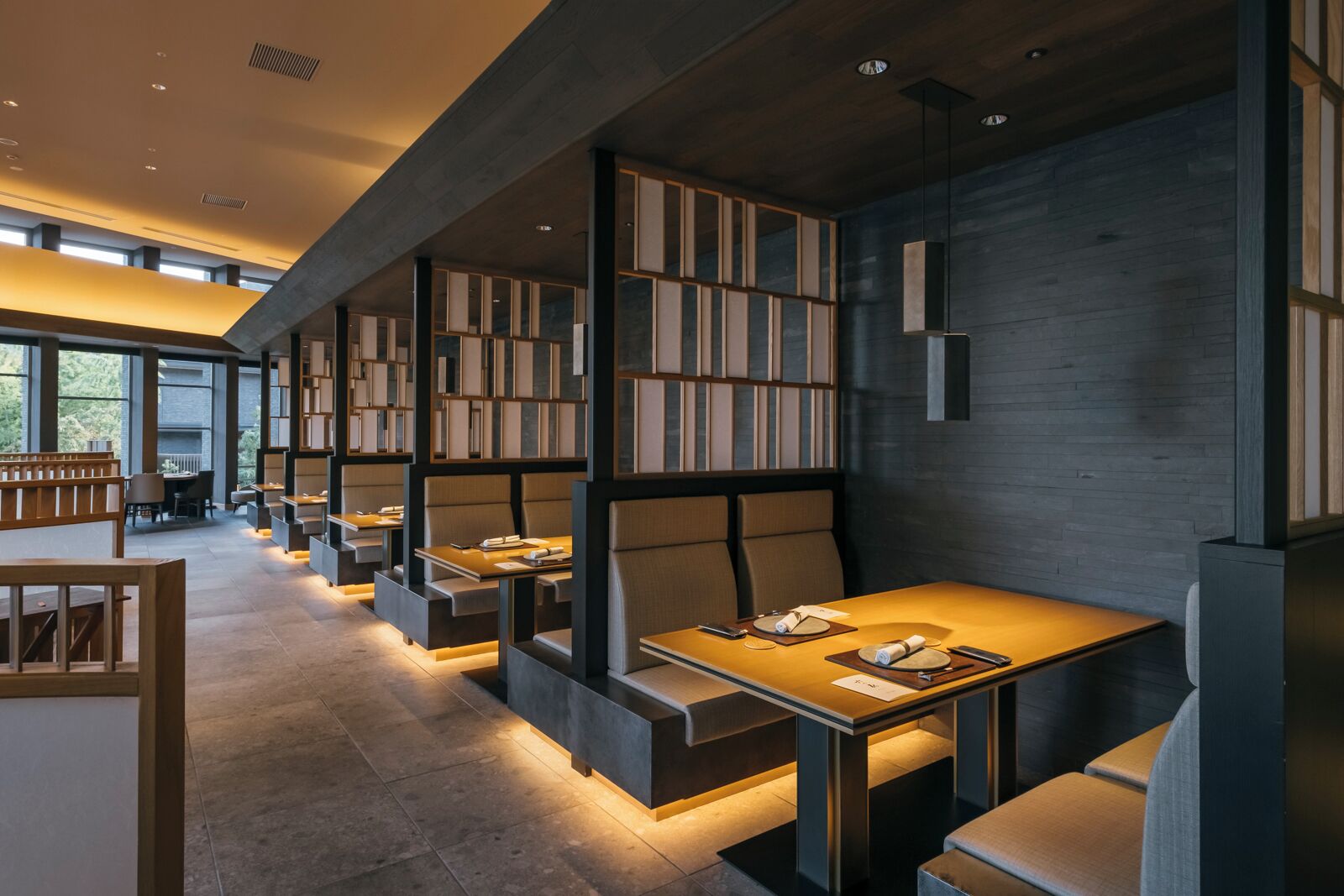 A modern restaurant with high tables and booths, wooden bookshelves, and a warm ambient lighting.