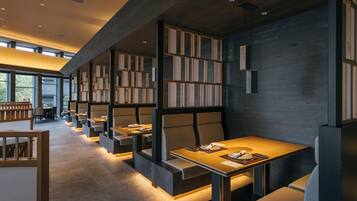 A modern restaurant with high tables and booths, wooden bookshelves, and a warm ambient lighting.