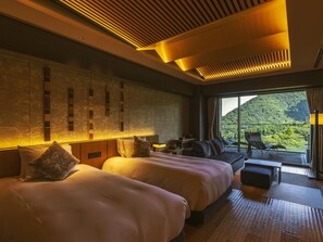 Habitación de hotel con dos camas, zona de estar y vistas a un paisaje montañoso.