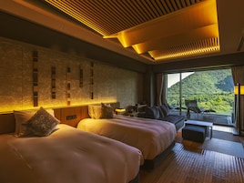 Habitación de hotel con dos camas, zona de estar y vistas a un paisaje montañoso.