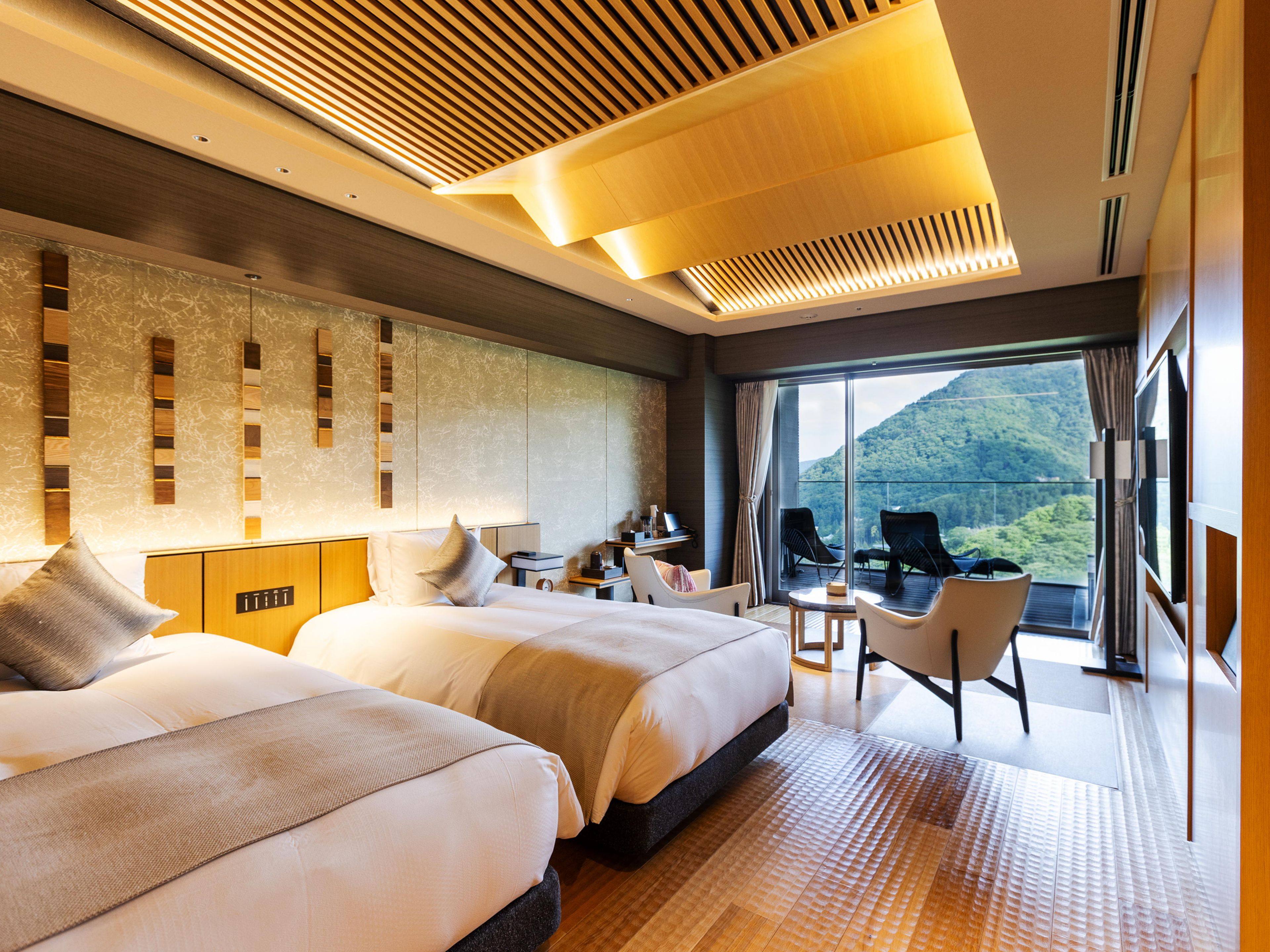 Une chambre d’hôtel moderne avec deux lits, un bureau et un balcon offrant une vue sur la montagne.
