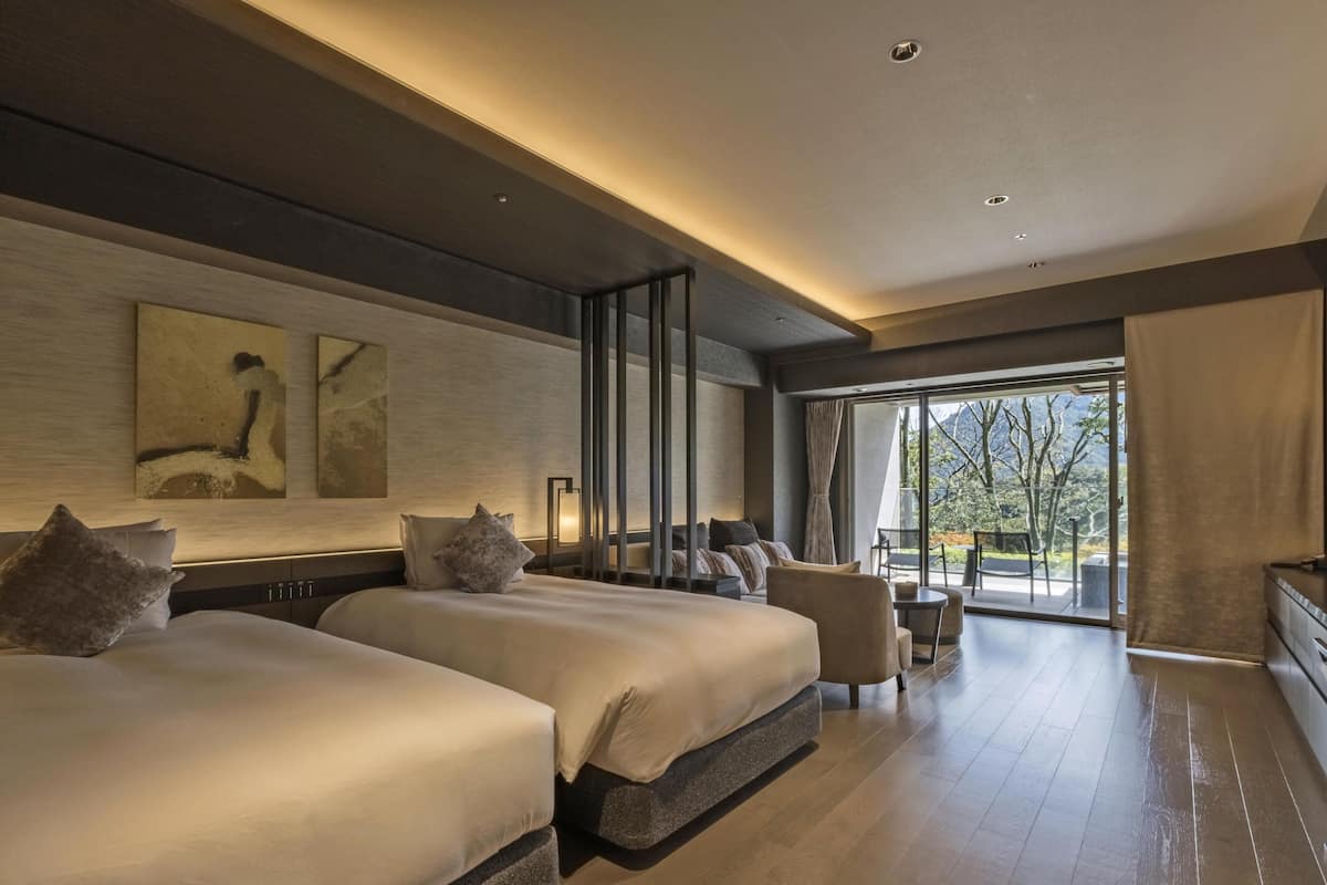 Ett modernt hotellrum med två stora sängar, en sittgrupp med bord och stolar samt ett stort fönster med utsikt över omgivningarna.