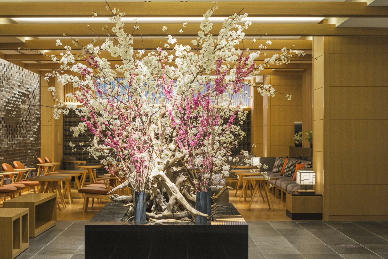 A lobby with a central floral arrangement, seating areas, and a brick wall.