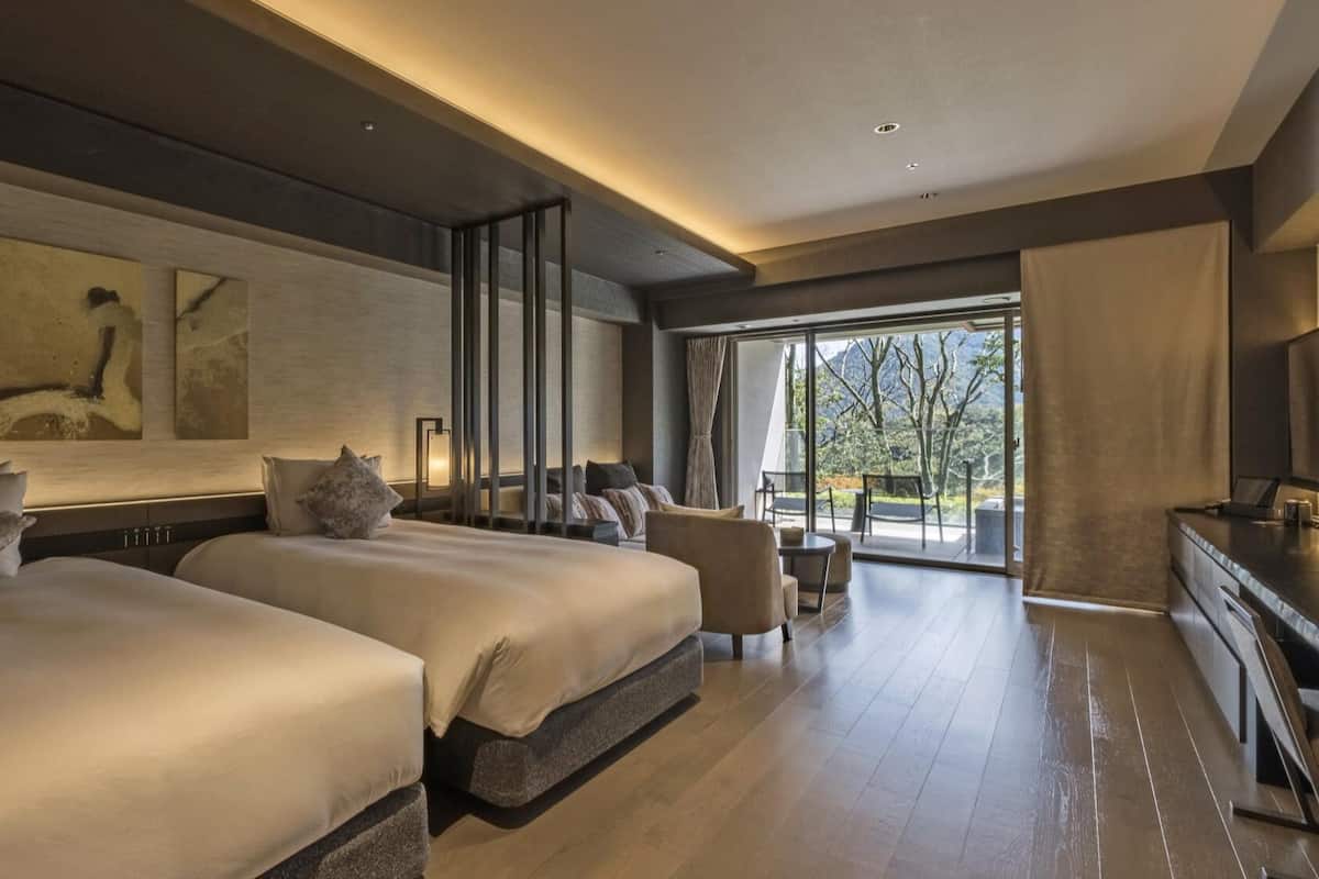 Ett modernt hotellrum med två sängar, en sittgrupp och ett stort fönster med utsikt.