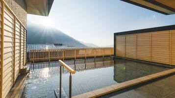 A traditional Japanese onsen with a wooden fence, a stone pathway, and a view of distant mountains.