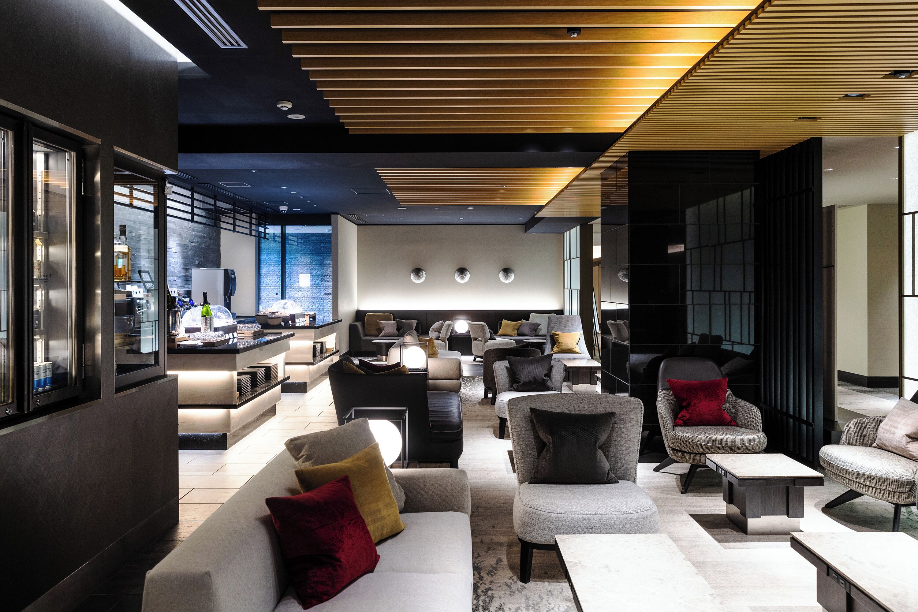 A modern lounge area with sofas, armchairs, and a bar area with bottles and glasses.