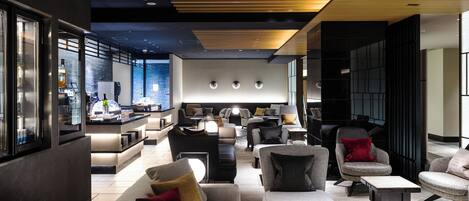 A modern lounge area with sofas, armchairs, and a bar area with bottles and glasses.