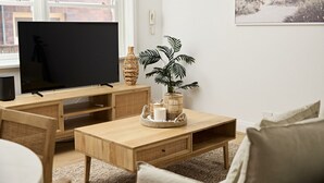 Un salon avec un téléviseur, des meubles en bois, une plante et un panier contenant des objets décoratifs.