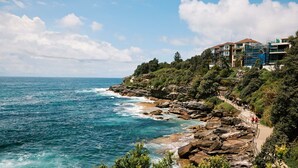 Un hôtel situé sur la côte, avec un rivage rocheux, une promenade pavée et une vue sur l’océan.