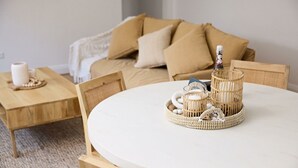 En hyggelig stue med et rundt hvidt bord, et træsidebord og en beige sofa med puder.