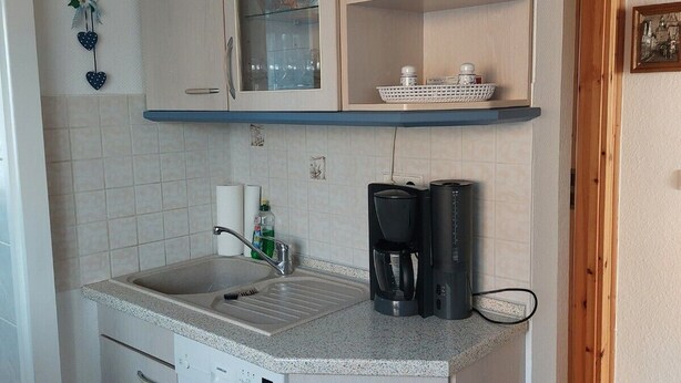 A compact kitchen with a built-in dishwasher, a coffee maker, and a shelf with baskets. - Vacation apartment in Liegau Augustusbad (Radeberg)