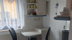 A small kitchen with a table and chairs, a radiator, and a window with curtains. - Vacation apartment in Liegau Augustusbad (Radeberg)