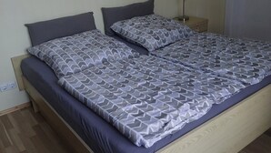 A double bed with a patterned bedspread and pillows, a wooden headboard, a nightstand with a lamp, and a wooden floor. - Vacation apartment in Liegau Augustusbad (Radeberg)
