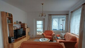 A living room with a wooden bookshelf, a television, a sofa, and a chair. - Vacation apartment in Liegau Augustusbad (Radeberg)