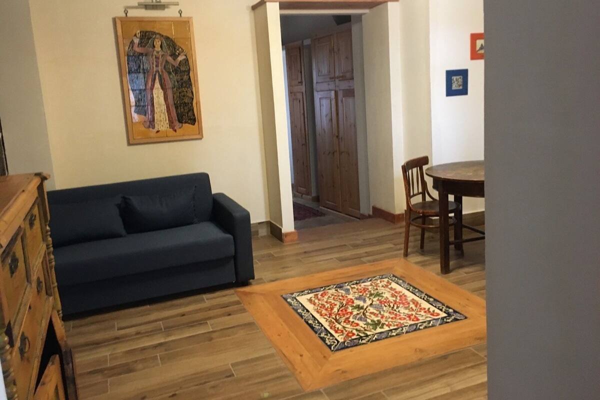 A living room with a dark blue sofa, a wooden coffee table with a floral rug, a wooden cabinet, and a painting on the wall.