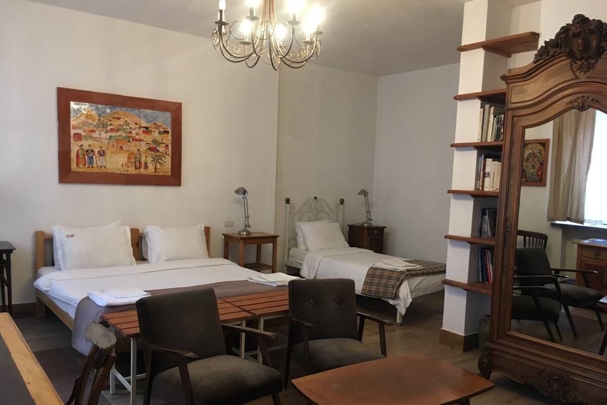 A hotel room with two beds, a wooden desk, a chair, a bookshelf, and a large mirror.