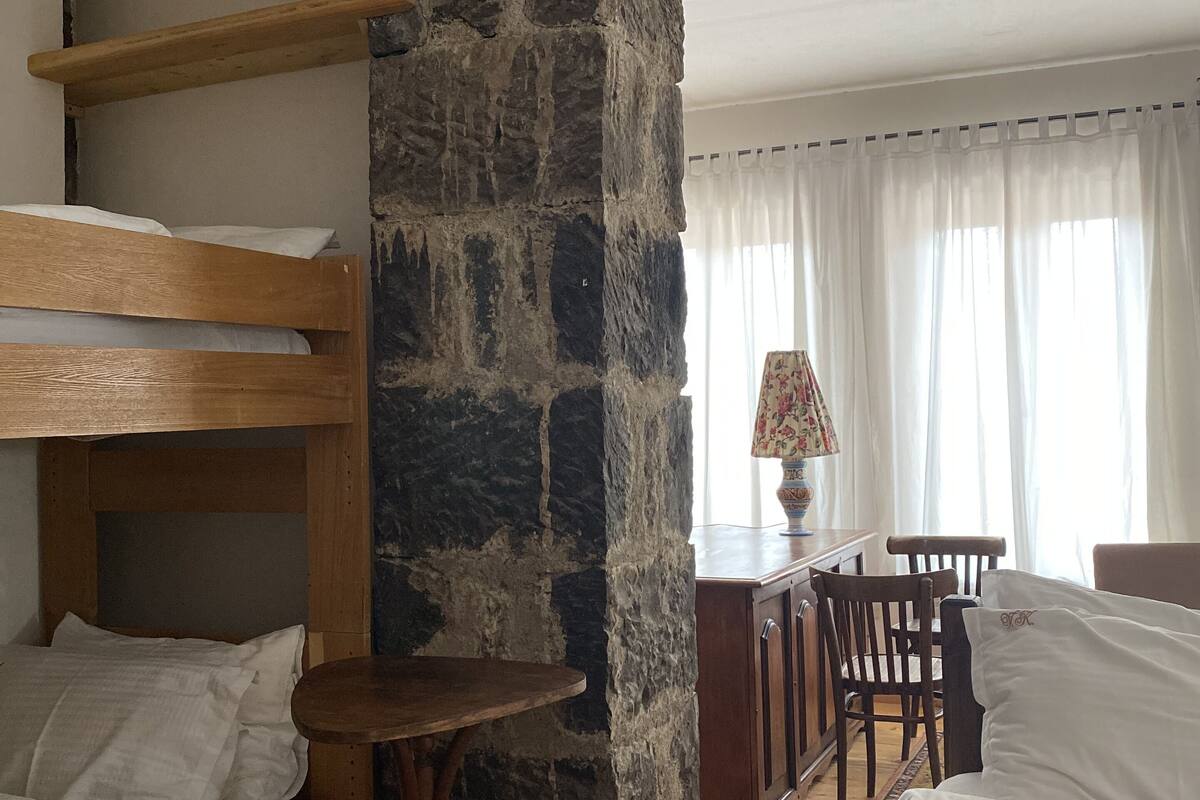 A room with a bunk bed, a stone pillar, a small table, a desk, and a chair.