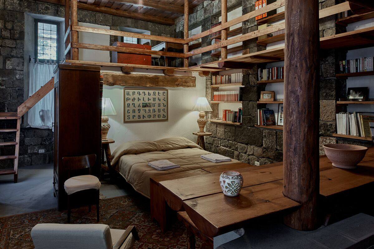 A rustic room with a wooden bed, a desk, and bookshelves filled with books.