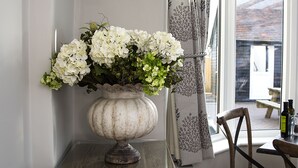 A white vase with flowers on a wooden table near a window with a curtain. - Maple Manor Hotel  (Crawley)
