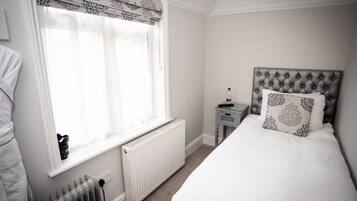 A bedroom with a bed, a nightstand, a radiator, and a window with curtains.