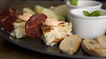 A plate with grilled meat, cheese, and bread, accompanied by small bowls of sauce and herbs.