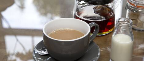 A cup of coffee on a saucer, a glass jar with a lid, and a small bottle of milk on a table.