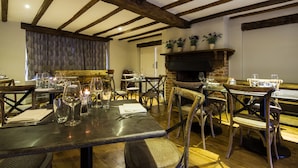 A restaurant with exposed wooden beams, brick fireplace, and tables set for dining. - Maple Manor Hotel  (Crawley)