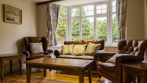 A room with a wooden floor, a brown leather sofa with patterned cushions, a wooden coffee table, and a brown leather armchair. - Maple Manor Hotel  (Crawley)