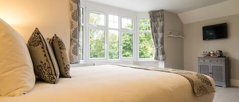 A bedroom with a large bed, a TV, and a window with curtains.