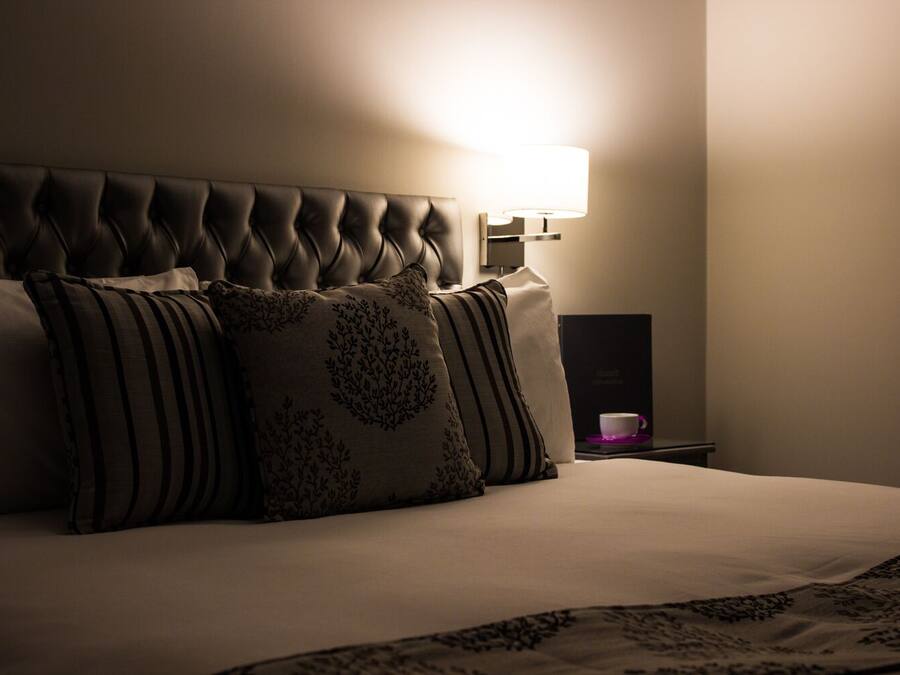 A neatly made bed with a tufted headboard, a bedside table with a lamp, and a cup on a saucer.