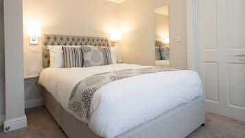A neatly made bed with a patterned bedspread, a tufted headboard, and bedside lamps.