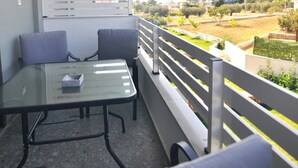 Un balcon avec une table en verre et deux chaises, une balustrade blanche et une vue sur un quartier résidentiel.