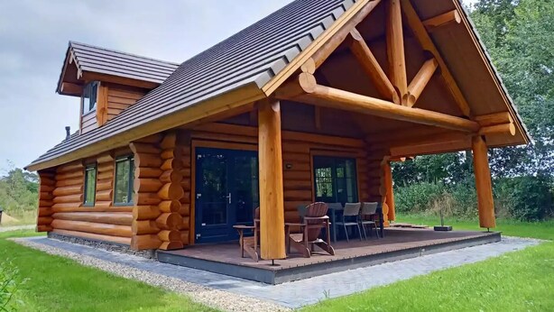 A log cabin with a covered porch and a dining area.