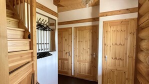A wooden staircase leading to a room with a chandelier, wooden doors, and a coat rack.