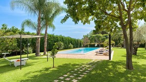 Un jardin avec une piscine, un espace salon couvert et un chemin en pierre.