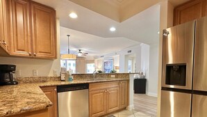 A modern kitchen with granite countertops, stainless steel appliances, wooden cabinets, and a tiled floor. - Belle Harbor  803-M - Panoramic Views (Clearwater Beach)