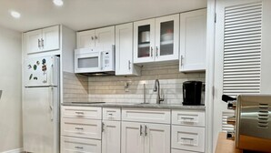 Een moderne keuken met witte kasten, een roestvrijstalen afzuigkap, een magnetron en een koffiezetapparaat.