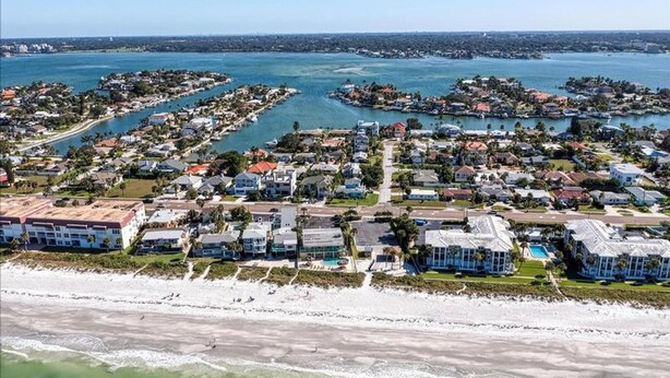 Luchtbeeld van een kustgebied met woonhuizen, een strand en een jachthaven.