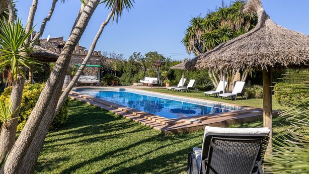 Un área de piscina con sillones de descanso y una sombrilla de paja.