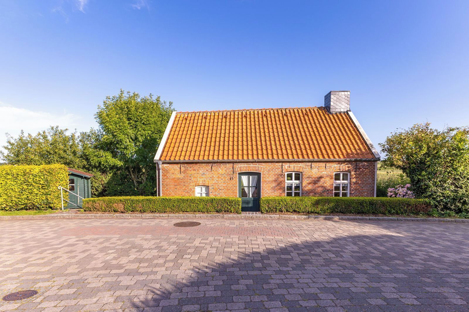 Une maison en briques avec un toit en tuiles, une porte verte et une petite dépendance attenante.