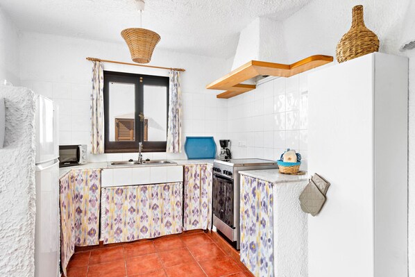 A compact kitchen with white tiled walls, a patterned backsplash, a microwave, a stove, and a sink.
