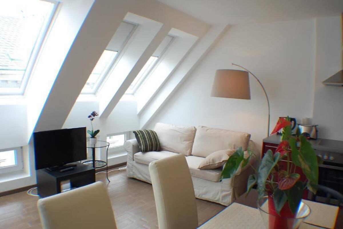 A modern loft apartment with a high ceiling, skylights, a sofa, a TV, and a dining area.