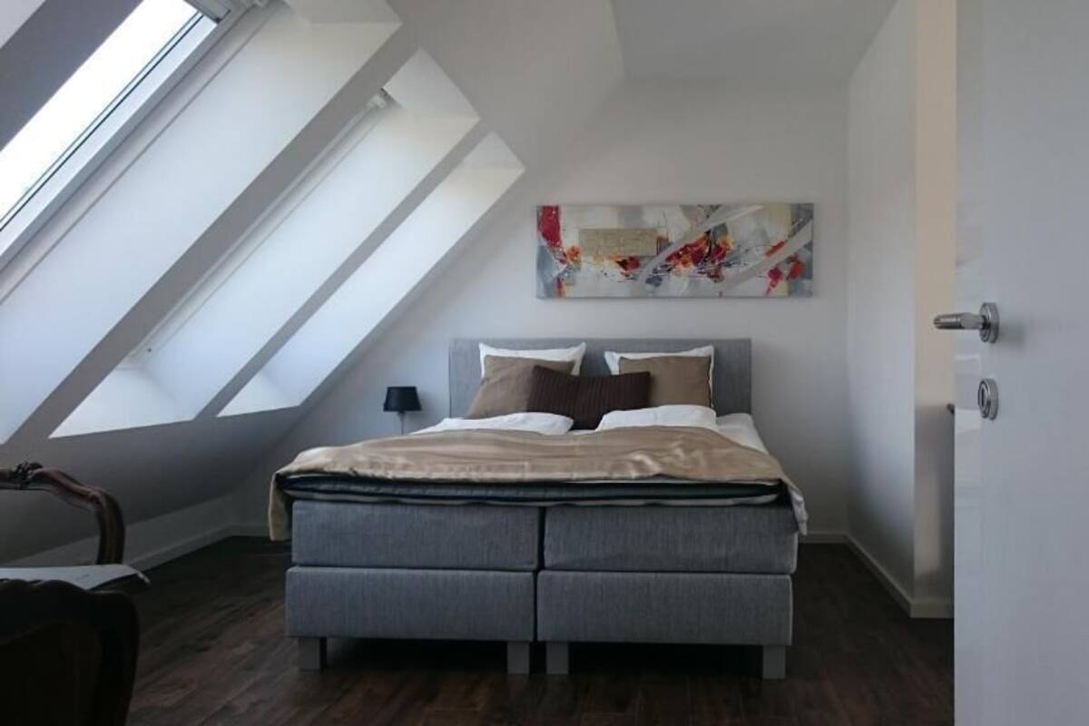 A bedroom with a skylight, a bed, a nightstand, and a painting on the wall.